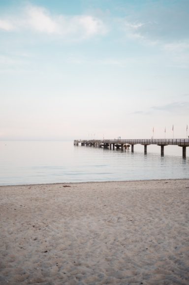 Fehmarn Ruhiger Strand mit einem Holzsteg, sanfte Wellen und ein klarer Himmel.