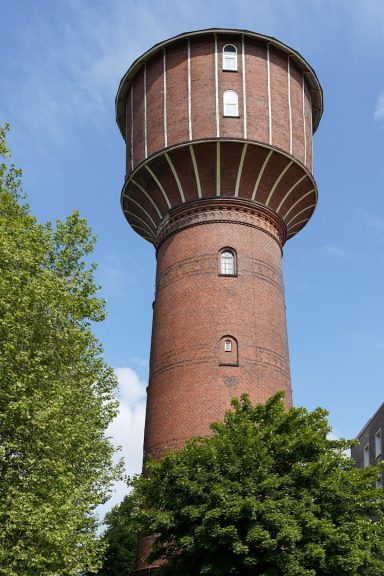 Elmshorn Ziegender, roter Wasserturm umgeben von Bäumen und klarem Himmel.