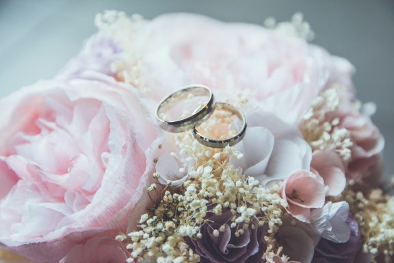 Hochzeiten Zwei Eheringe liegen auf einem Blumenstrauß mit rosa und weißen Blumen.