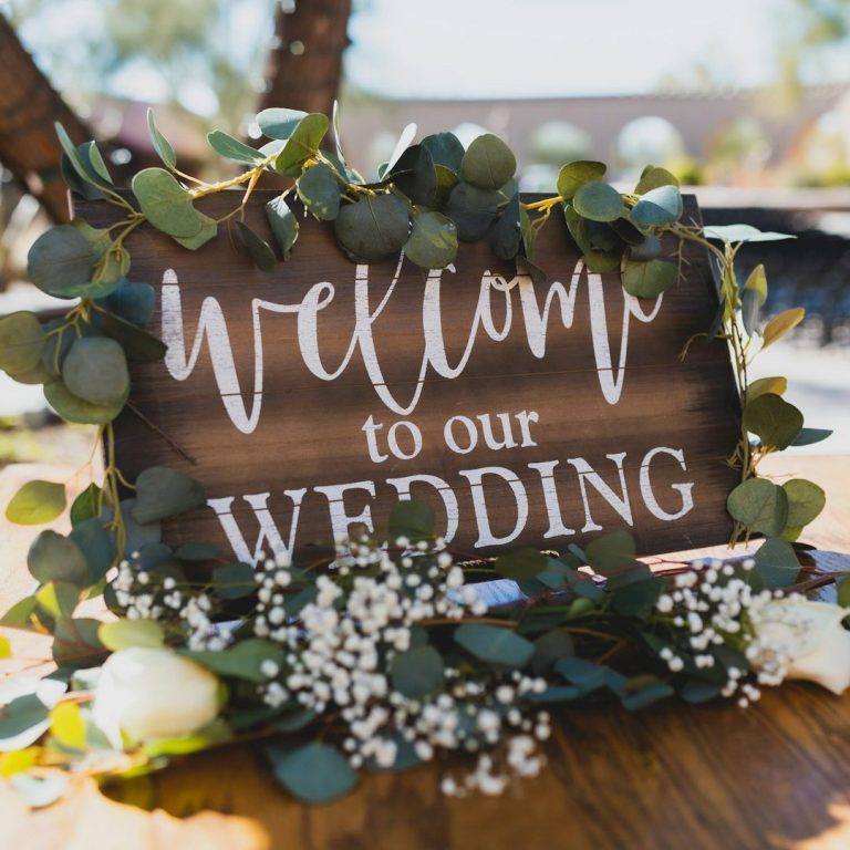 Sind alle auf der Hochzeit Willkommen? Willkommensschild für eine Hochzeit, umgeben von grünen Blättern und Blüten.