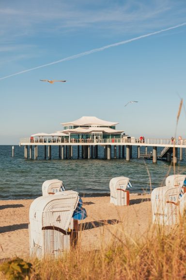 Timmendorfer Strand Blick auf einen Steg mit Möbeln am Strand und einem klaren blauen Himmel.