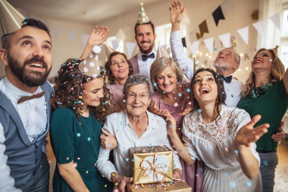 Familienfeiern Gruppenfoto von feiernden Menschen mit Geschenken und Konfetti in fröhlicher Atmosphäre.