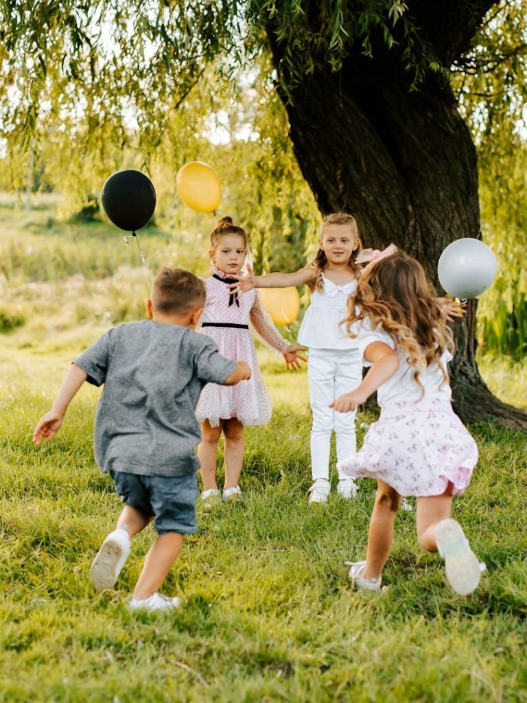Spaß für Kinder auf Veranstaltungen Vier Kinder spielen mit Luftballons unter einem Baum auf einer Wiese.