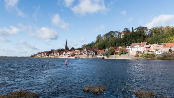 Lauenburg/Elbe Landschaft mit einem See, einer Stadt am Ufer und bewaldeten Hügeln im Hintergrund.