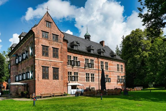 Reinbek Historisches Gebäude mit roten Ziegeln, grüner Wiese und wolkigem Himmel.